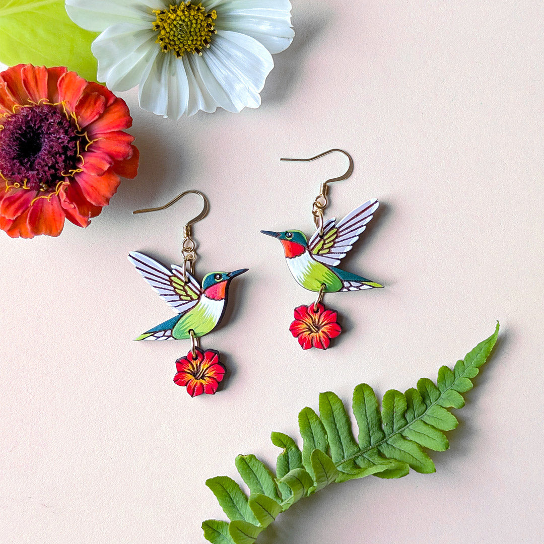 Colorful hummingbird and red flower earrings with flowers and a fern leaf on a light background
